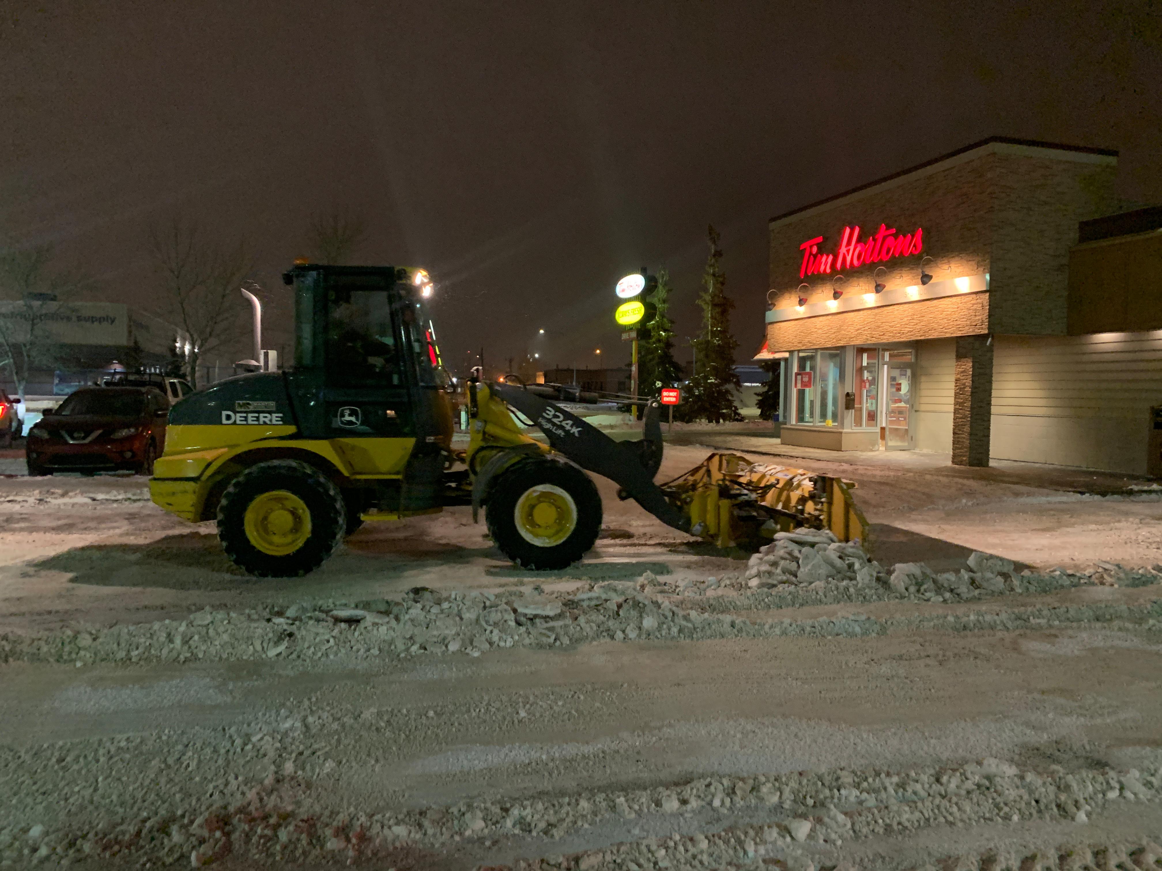 John Deere wheel loader plowing snow at night in commercial parking lot
